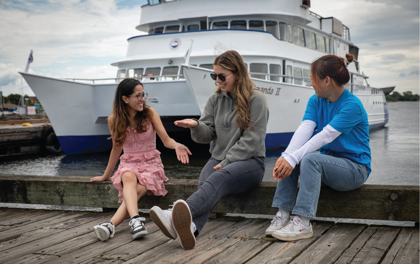 3 students sitting on the pier in front of the Chief Commanda II