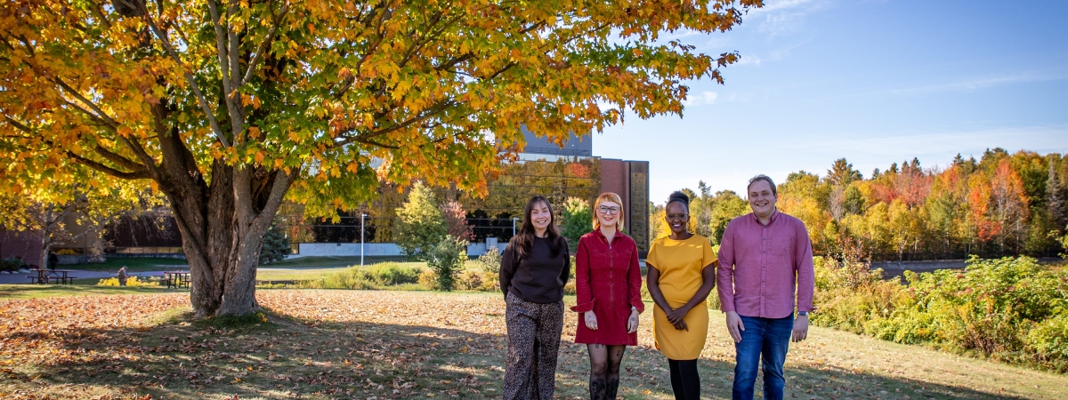 A group of people in front of a fall tree behind the Nipissing building.