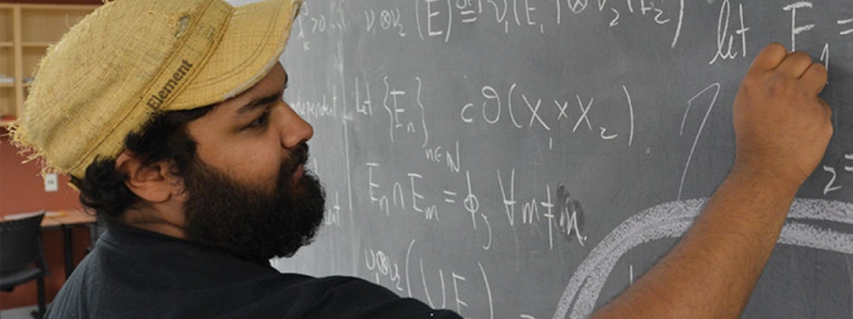 A student in black t-shirt writing math equations on the blackboard