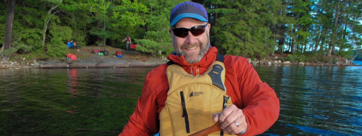 Terry Dubroy smiles at the camera from his canoe with a forested background.