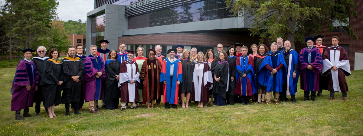 The entire Nipissing faculty of arts and science in convocation gowns standing in a group in front of the library background