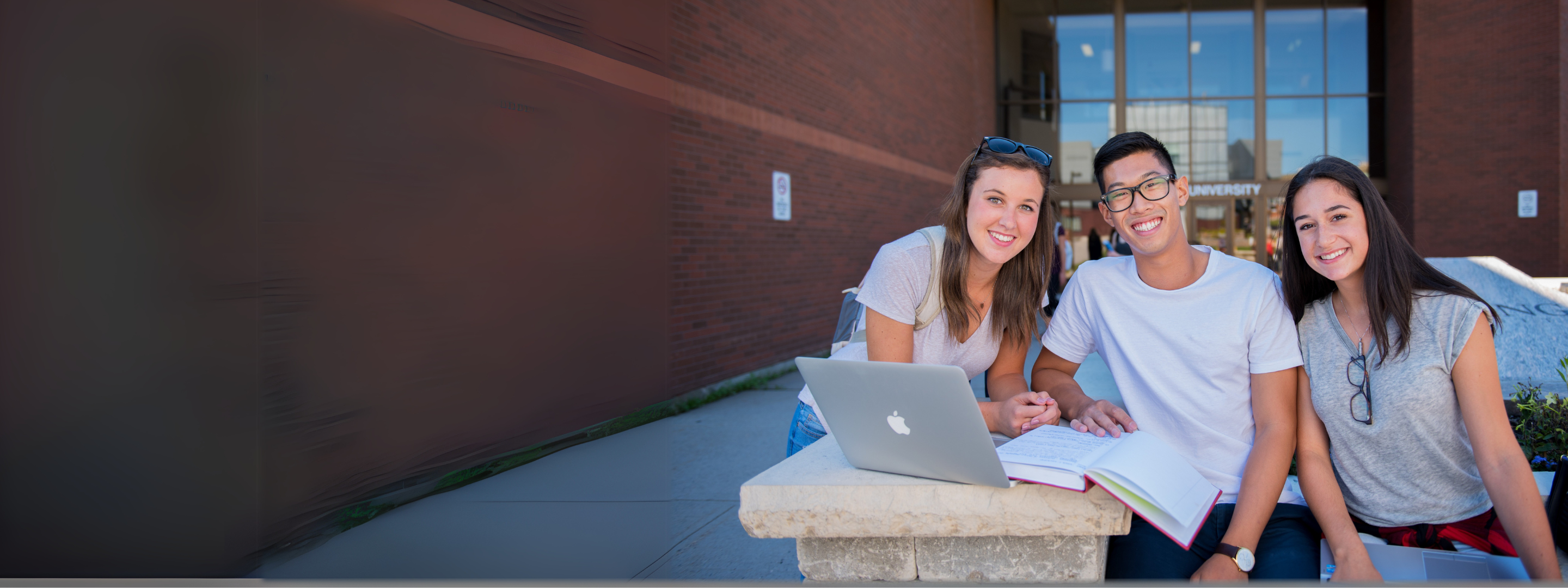 3 students sitting at the university front entrance
