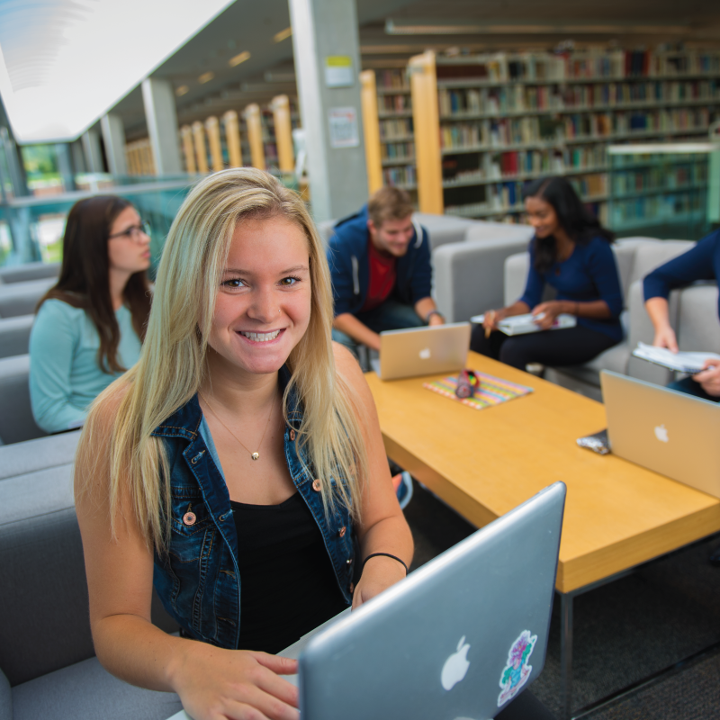 A student with her laptop while the students in the background are chatting