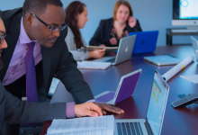 School of Business associates sit around a board table analyzing data on computers.