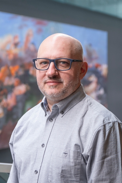 A man in gray shirt standing with the interior background of the library in view