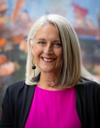 A woman in pink and black top in front of a colorful background
